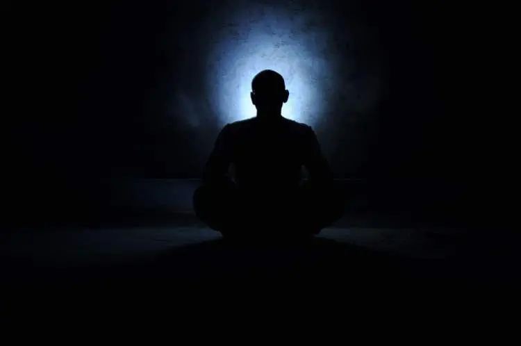 Spiritual journey of a man meditating in darkness.