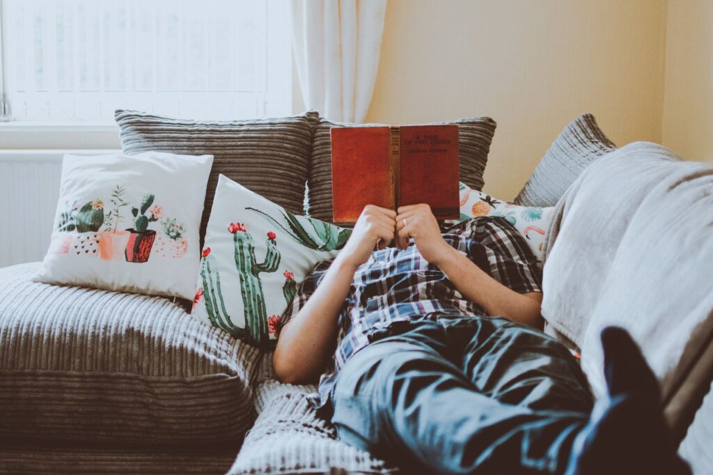 An example of a man who is in his comfort zone. He lying on the sofa is reading a book.