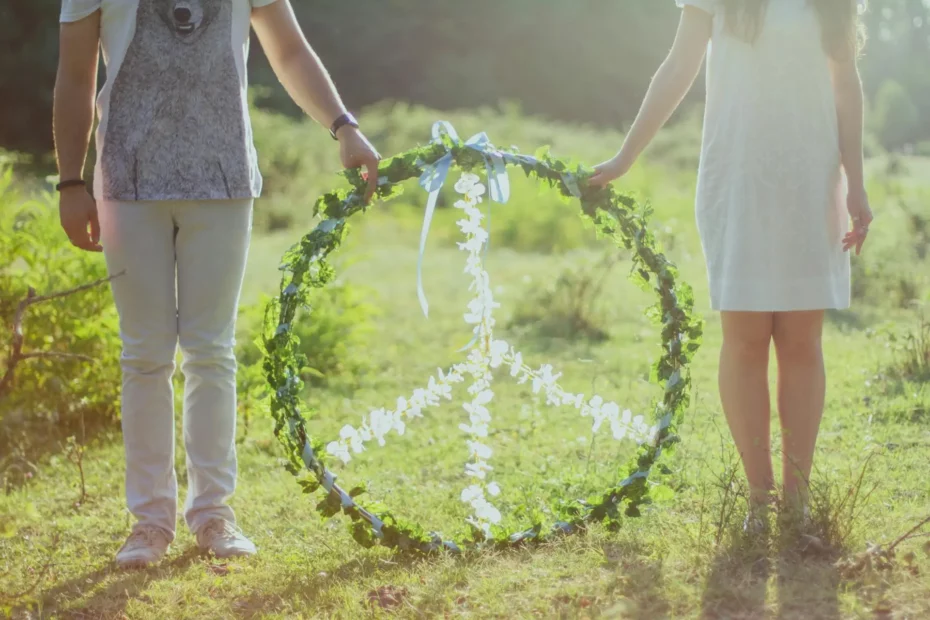 Peace sign made from natural elements, held by a man and a woman in a white dress, standing on grass with trees in the background.